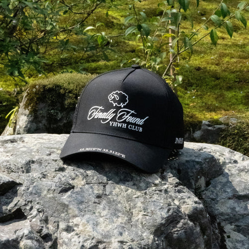 Black cap with white text on a rock with greenery in the background