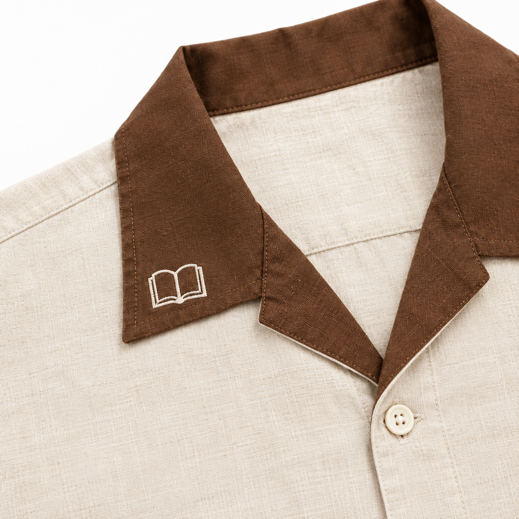 Detalle del cuello color marrón en contraste de la camisa beige LUMBRERA: LIGHT, con bordado de un libro abierto