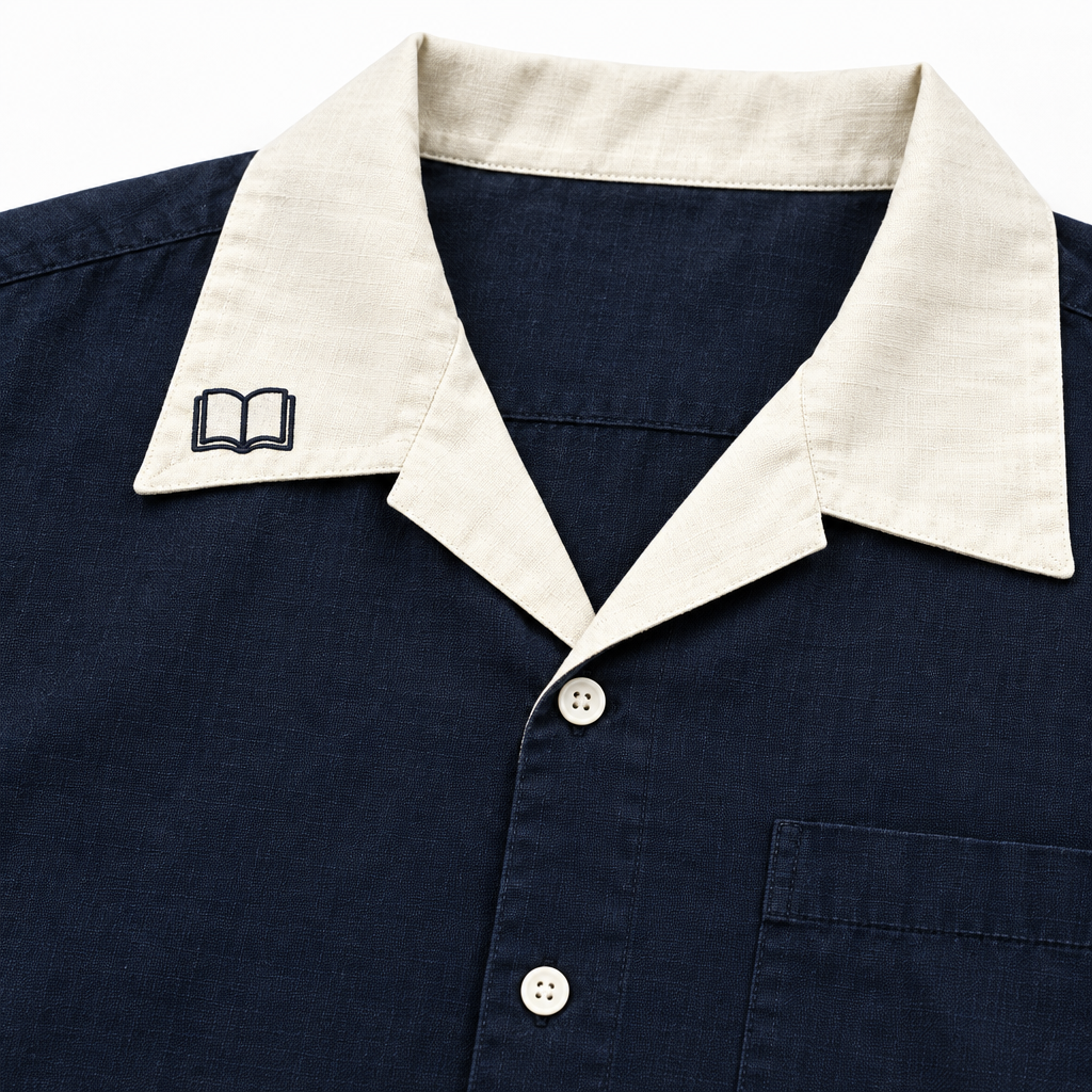 Detalle del cuello color crema en contraste de la camisa azul oscuro LUMBRERA: SHADOW, con bordado de un libro abierto